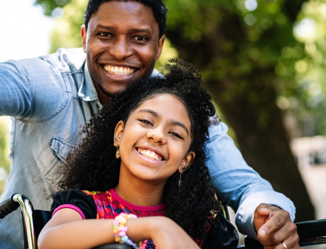 a male and her daughter sitting on a wheelchair